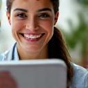 A confident, professional female wellness coach smiling and addressing a client via a virtual call on a tablet, demonstrating personalized support.